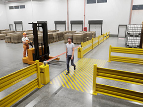 Pedestrian crossing a striped walkway between AisleCop gates while a forklift waits behind a lowered gate arm