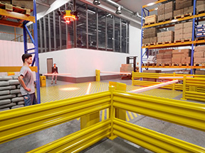Pedestrian waiting at yellow AisleCop gates at an intersection of several forklift aisles under an overhead warning light
