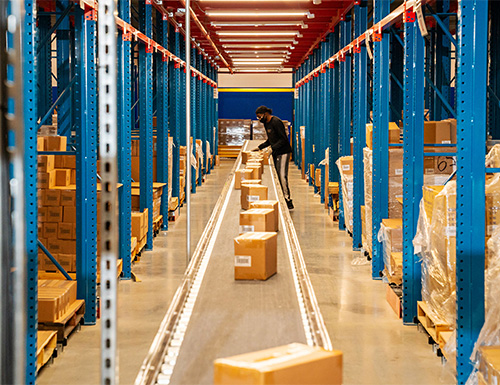 worker placing carton on conveyor in aisle between pallet racks